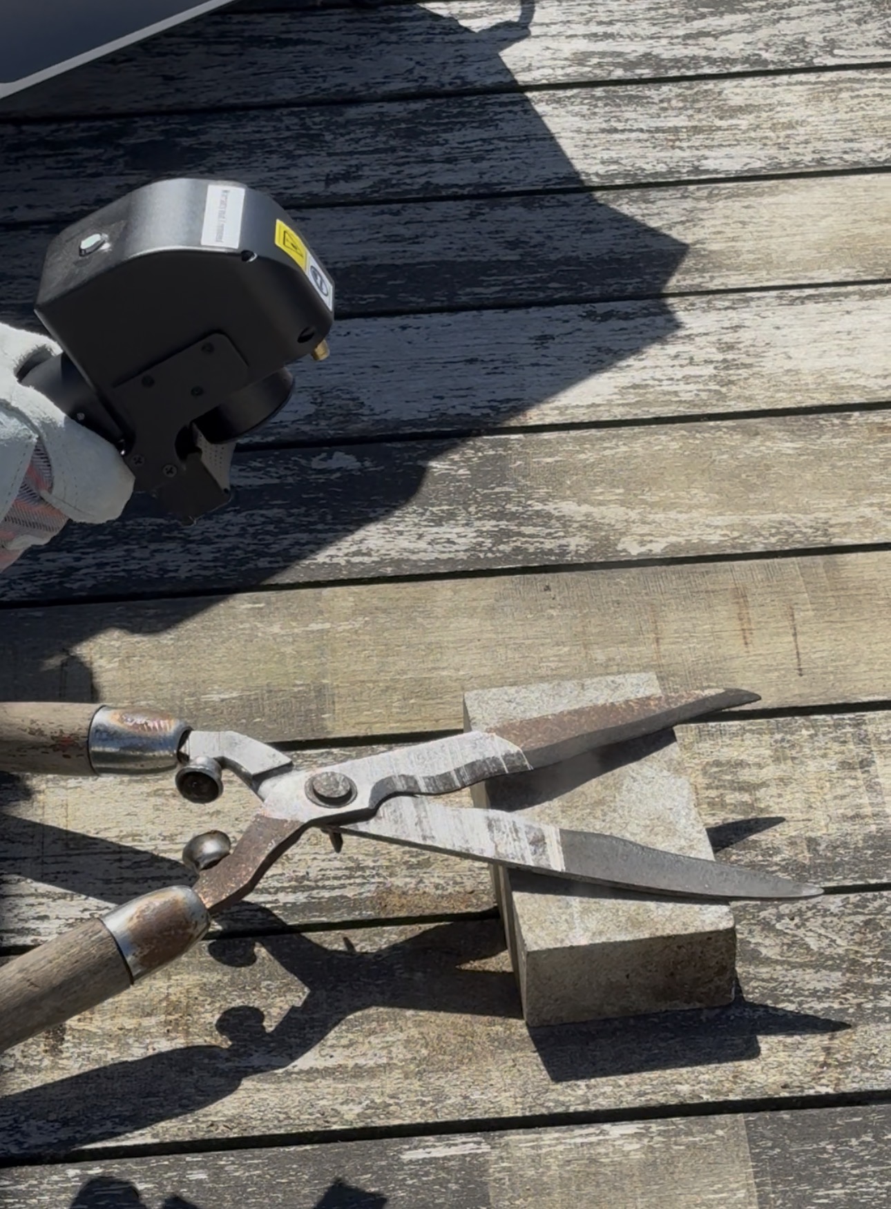 Laser cleaning rusted garden shears on a weathered wooden deck